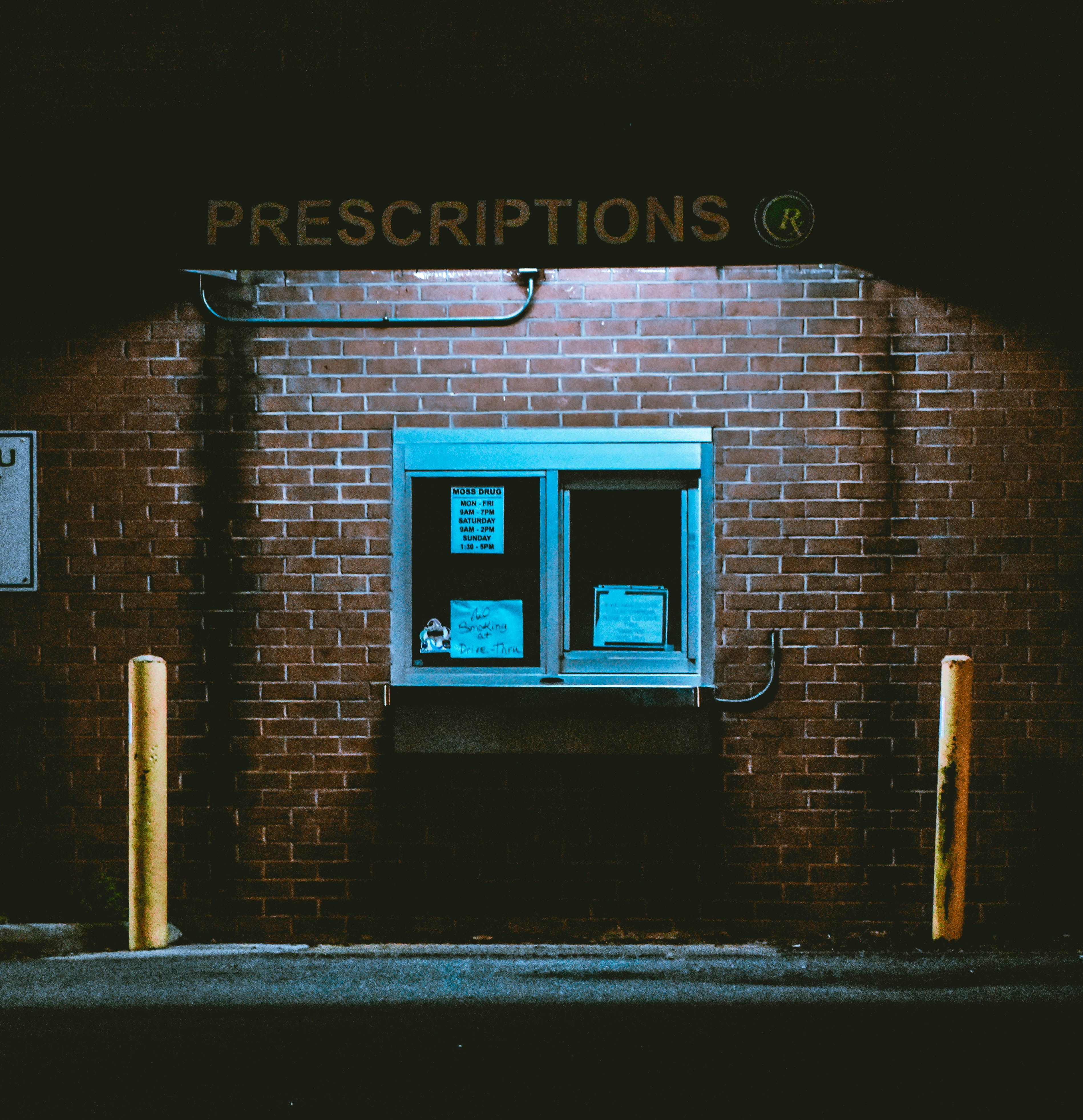 A dead pharmacy illuminates it's drive through window during the dark of night.